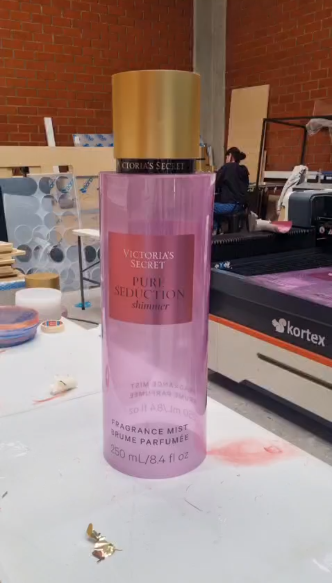 Cylindrical translucent pink and purple mica perfume display dummies with matte gold caps and central pink labels shown inside a workshop.