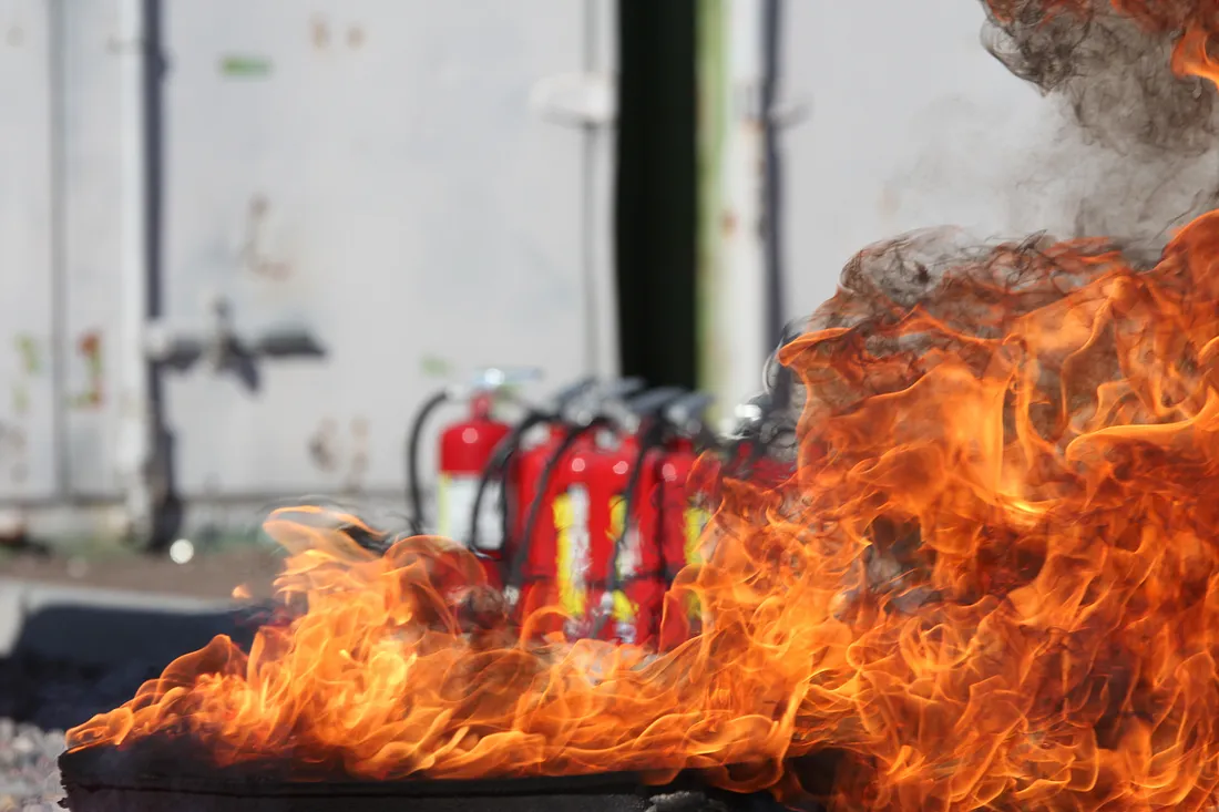 A raging fire with unused fire extinguishers in the background.