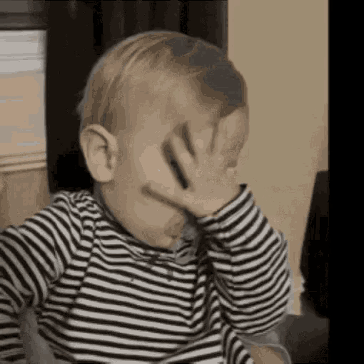a baby wearing a striped shirt is covering his face with his hand