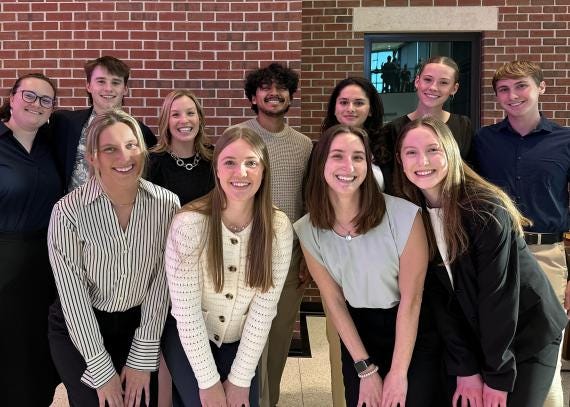 A group of students pose for a photo against a red brick building.