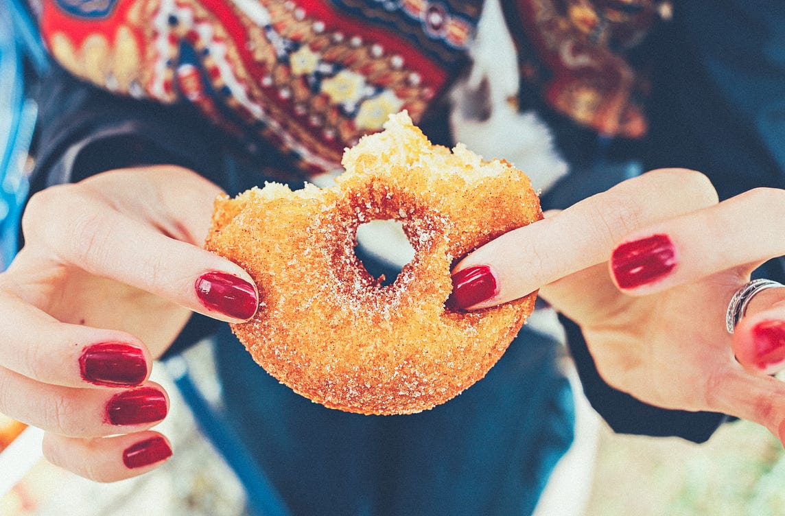 Hands with red nail polish clutch a half-eaten donut.