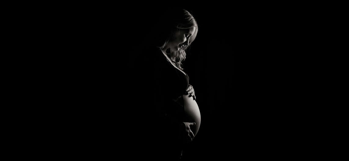Pregnant young woman looking down at her bump which she is cradling with her hands.