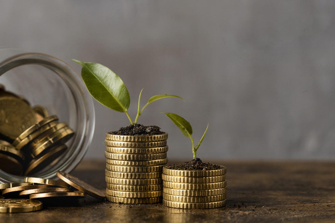 Two piles of gold coloured coins with small green seedlings growing out of the top.