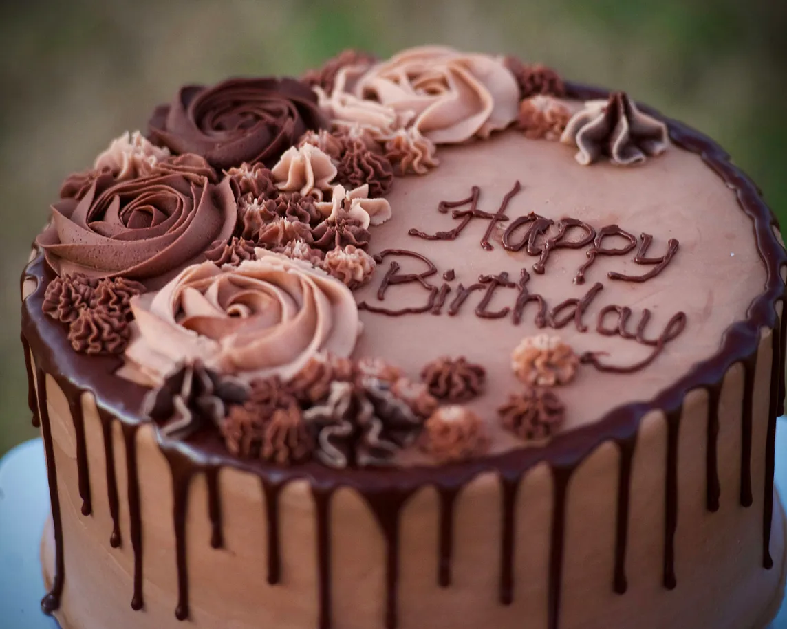 A chocolate frosted cake with rosettes saying “happy birthday”