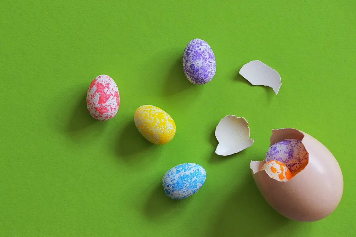 A cracked eggshell, with multiple smaller eggs inside and spilling out of it, in multiple colours