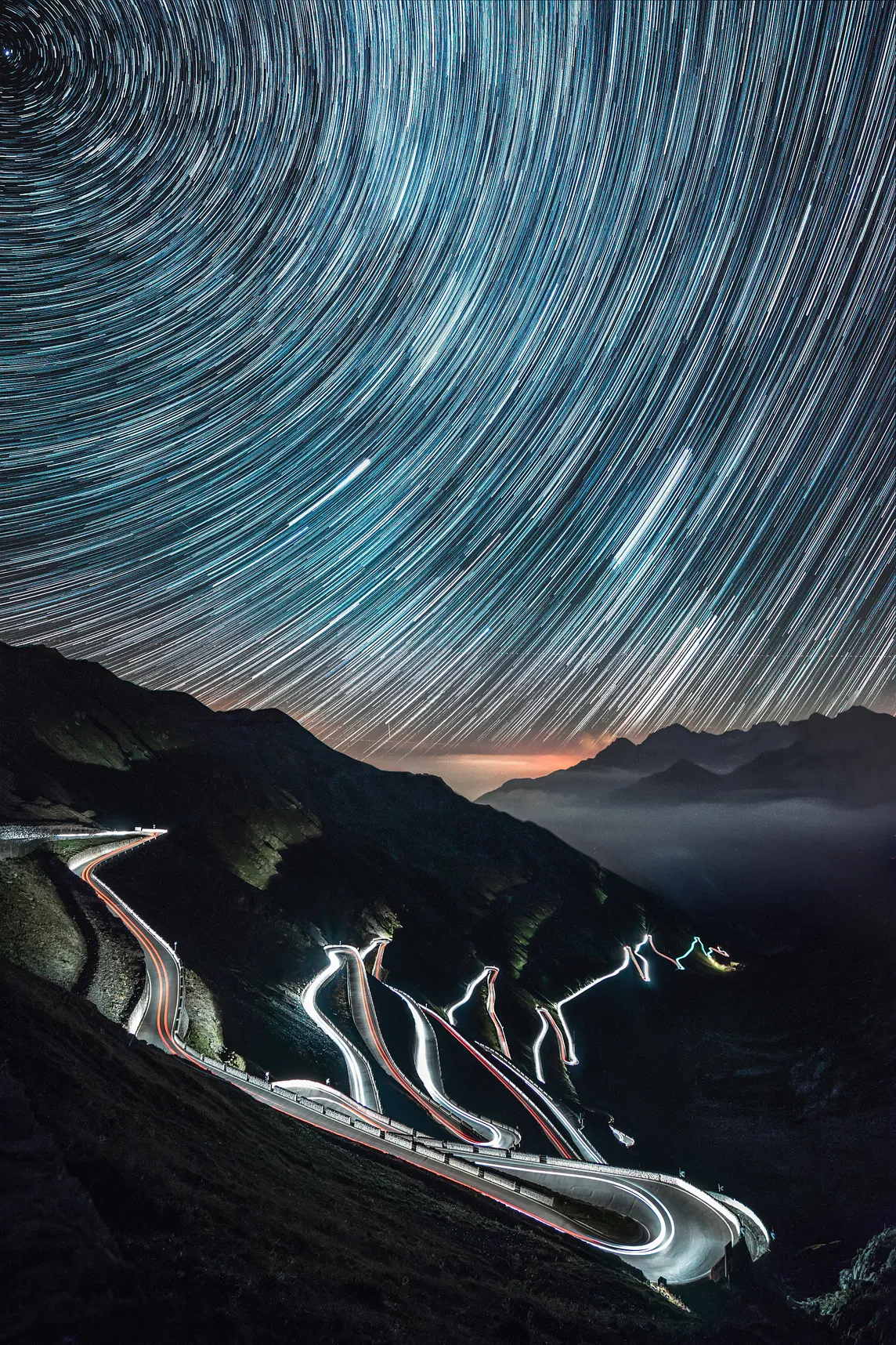 Unusual time lapse photograph of stars rotating in streaks around the zenith over vehicles lights time lapse streaking down a mountain switchback.