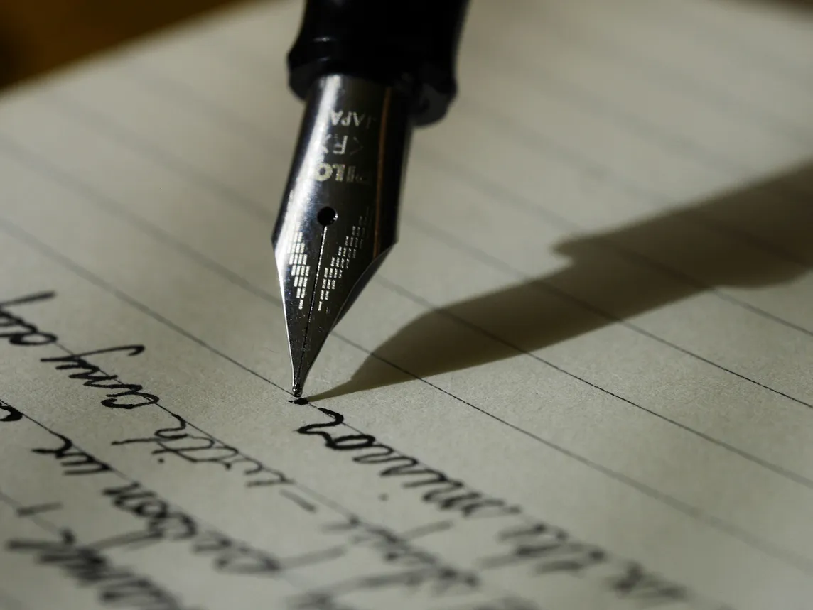 an image of an old school ink pen with cursive writing on lined notebook paper