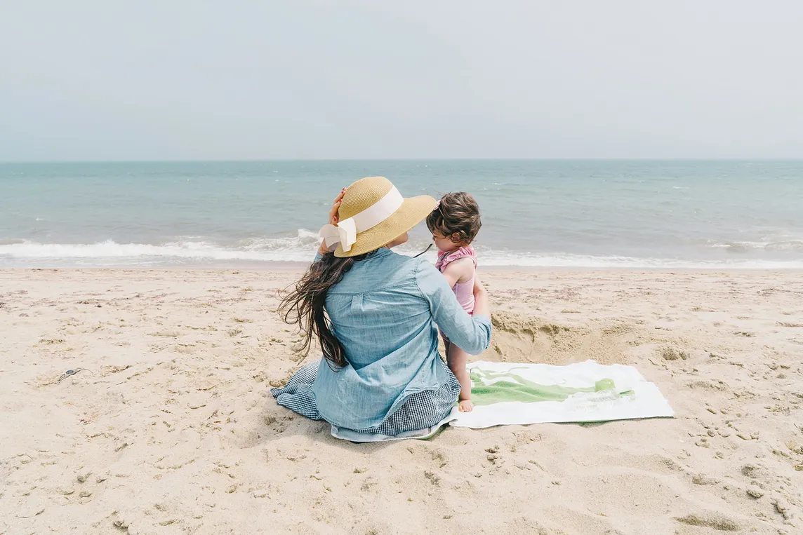 Woman relaxing on the beach holding a baby.