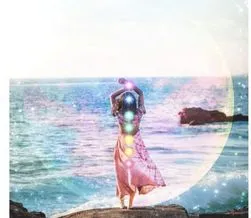 woman with a pink dress standing near the ocean and her back highlights the chakras