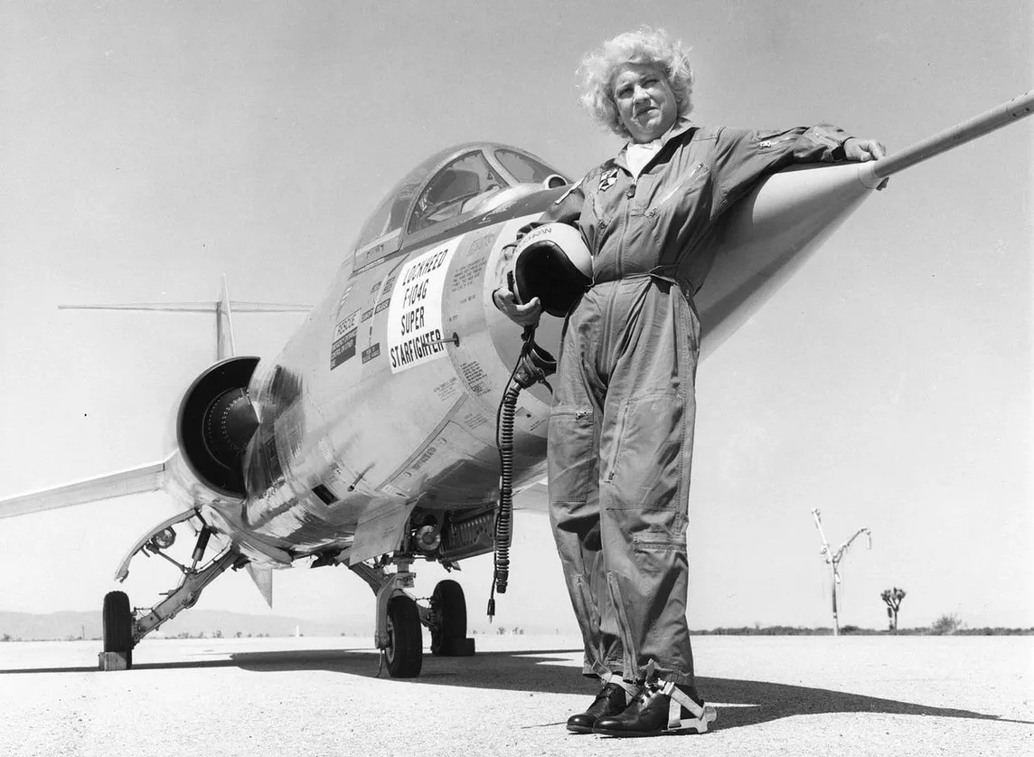 Black and white Photo of Jacqueline Cochran in flying uniform standing in front of Lockheed F-104G Super Starfighter plane on runway. Posted on mickey markoff 2024 article on women in aviation; credit — US San Diego Air & Space Museum