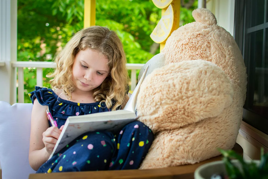 A young girl with a large teddy bear writing in a book