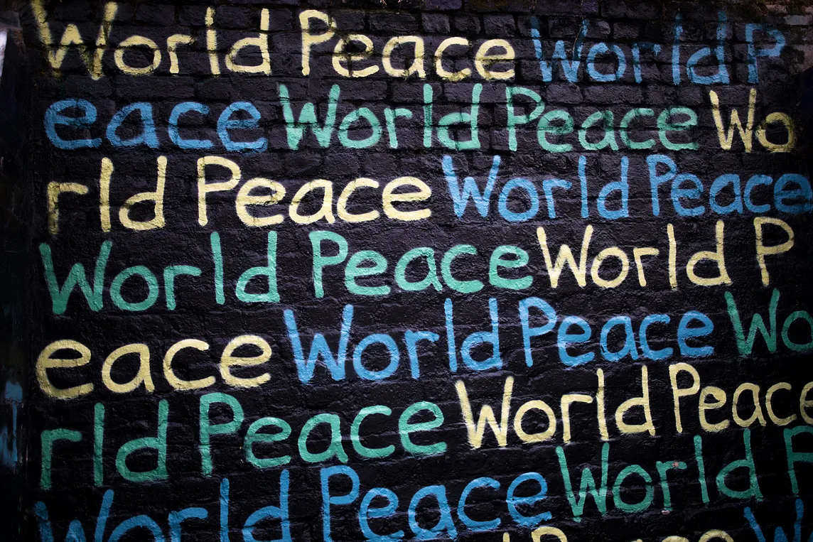 The words World Peace written repeatedly on a black painted wall.