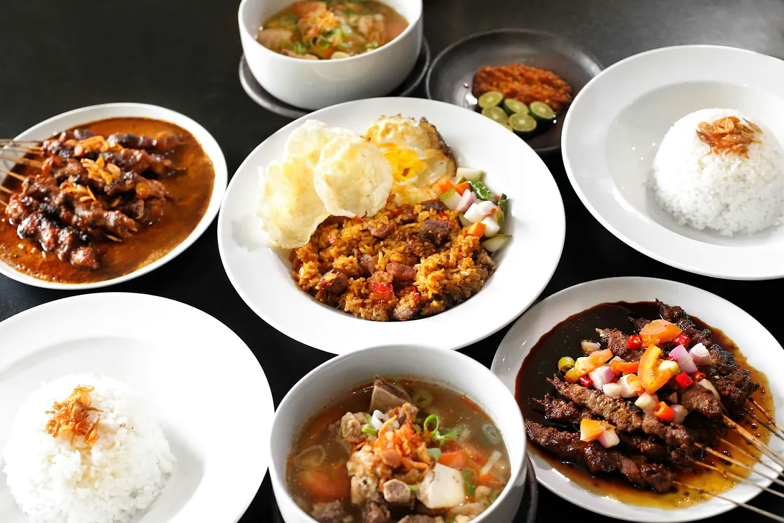 Various plates of food including rice, skewers of meat, soups and curries