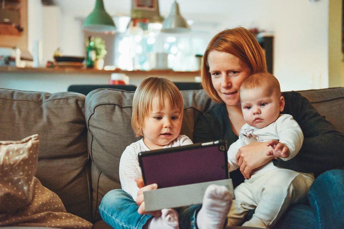 Mother watching an iPad with two children: a todler and a baby