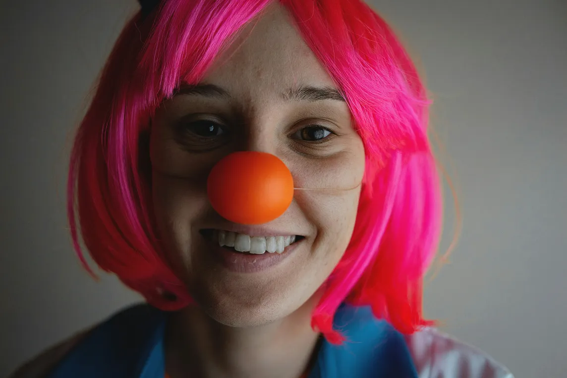 A smiling girl with a clown’s nose cap.