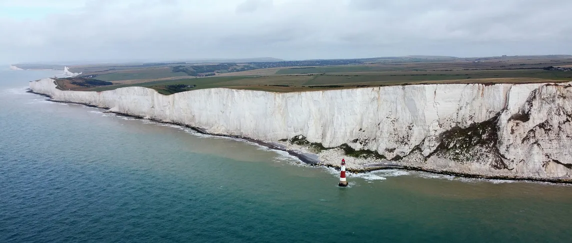 The long stretch of Beachy Head’s cliffs dwarfs the red and white lighthouse in the sea below.