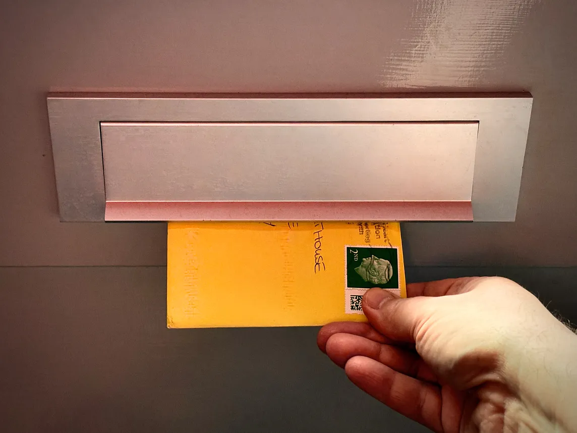 A hand grabbing a yellow envelope coming through a letterbox.