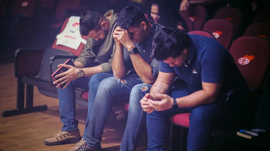 A trio of football-like guys are praying in a church-like surrounding.