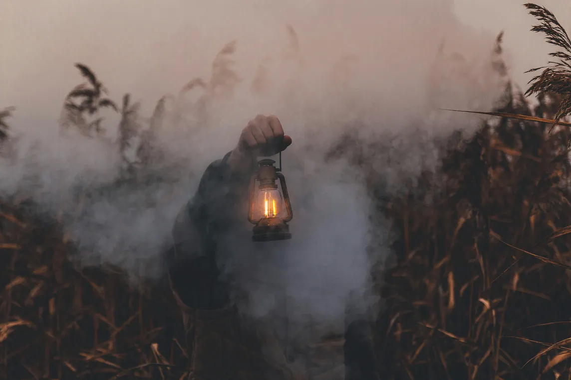 An arm holding a kerosene lantern. There’s a person hidden in the smoke, and it’s not quite clear where they should be going.