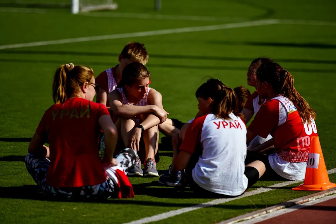 A group of youth soccer players rest on a turf field.