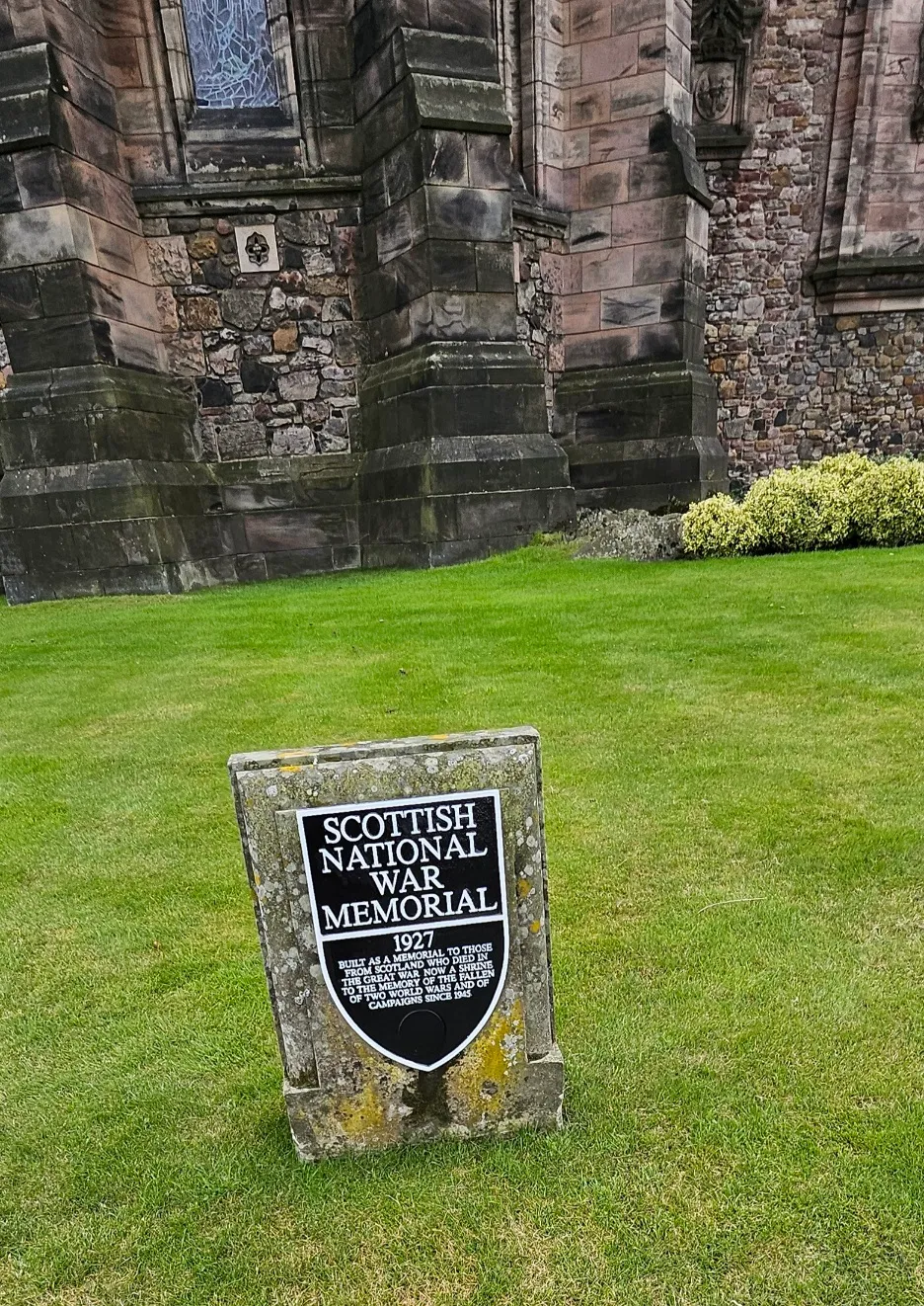 The rear of the War Memorial with a commemorative plaque set on the grass in the foreground. It states “Scottish National War Memorial. 1927. Built as a memorial to those from Scotland who died in the Great War. Now a shrine to the memory of the fallen of two world wars and of campaigns since 1945