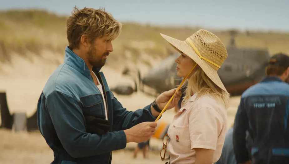 A blonde man in a blue jumpsuit holds the strings on a hat worn by a blonde woman. Fall Guy movie review, action, comedy