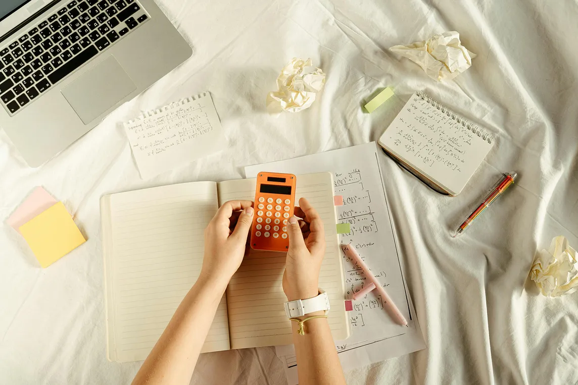 A woman holding a calculator. A notebook and pen are nearby.