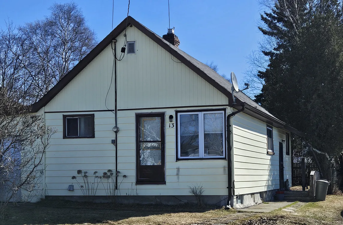 A small bungalow, painted yellow. Brown trim and a white garage door.