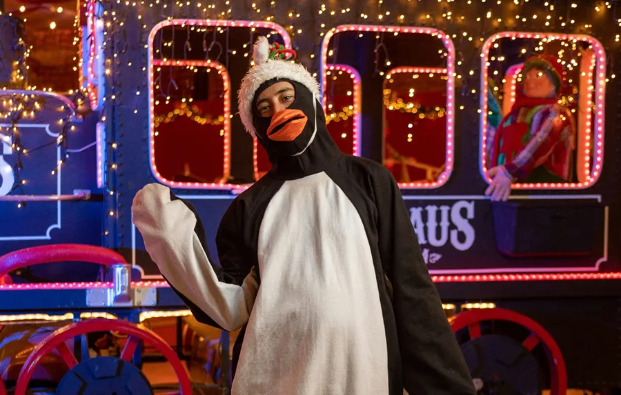 Person in penguin costume standing by carnival train.