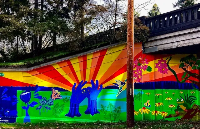 A birghtly colored mural depicting the flush of Spring. Flowers, wildlife and streams of orange and yellow sun illuminating the background