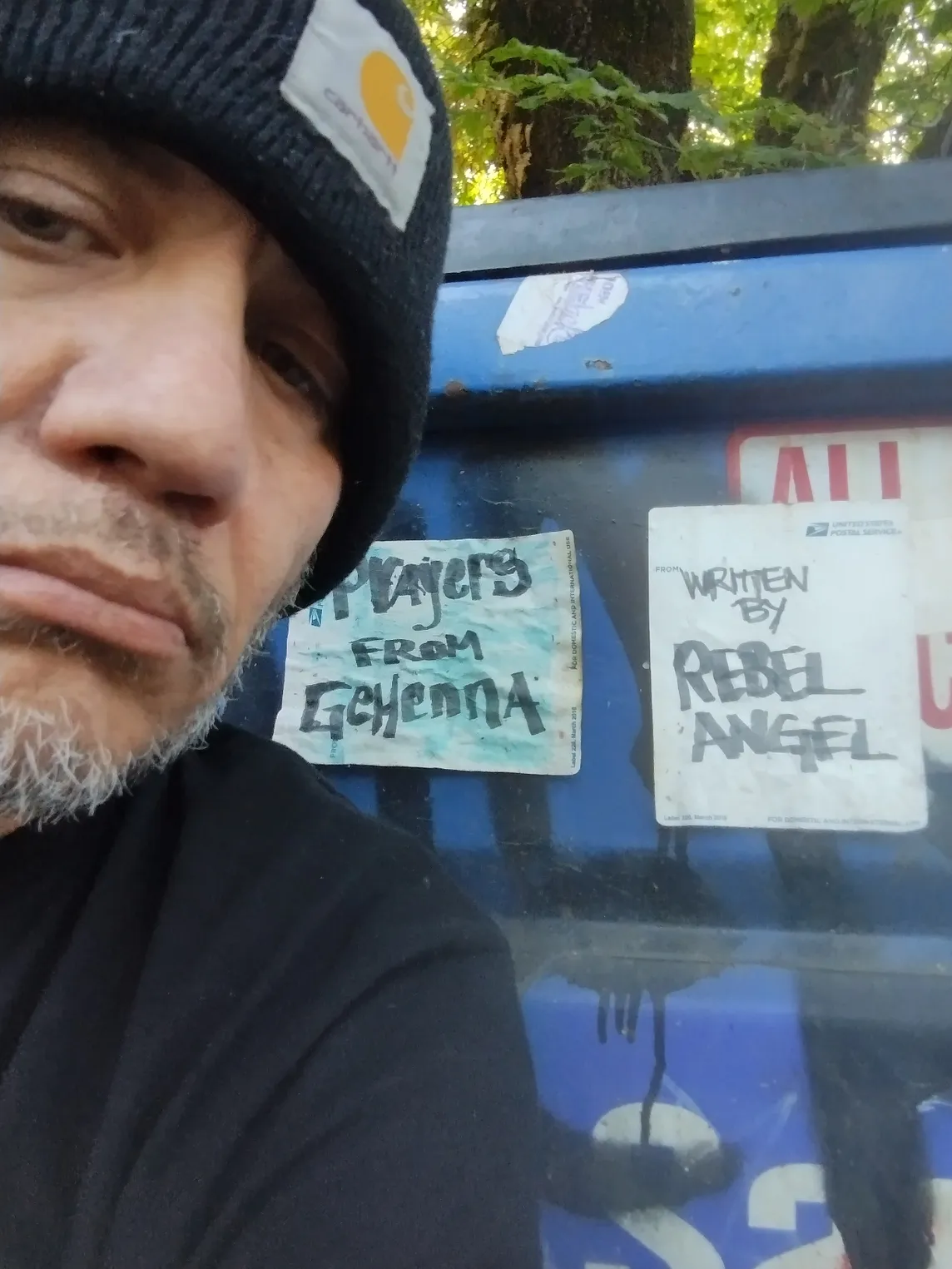 An unfortunate looking man squats beside a dumpster