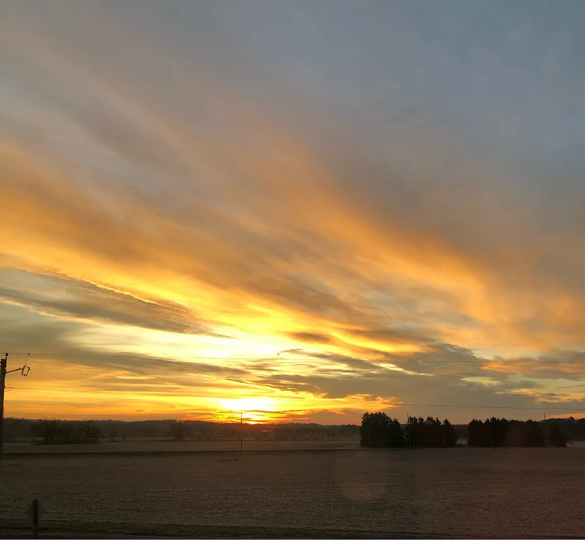 Sunrise on a fall morning. Clouds reaching out like fingers spanned sun shining behind the clouds still darkness. Sky colors gray, yellow, white. Looks like Heaven.