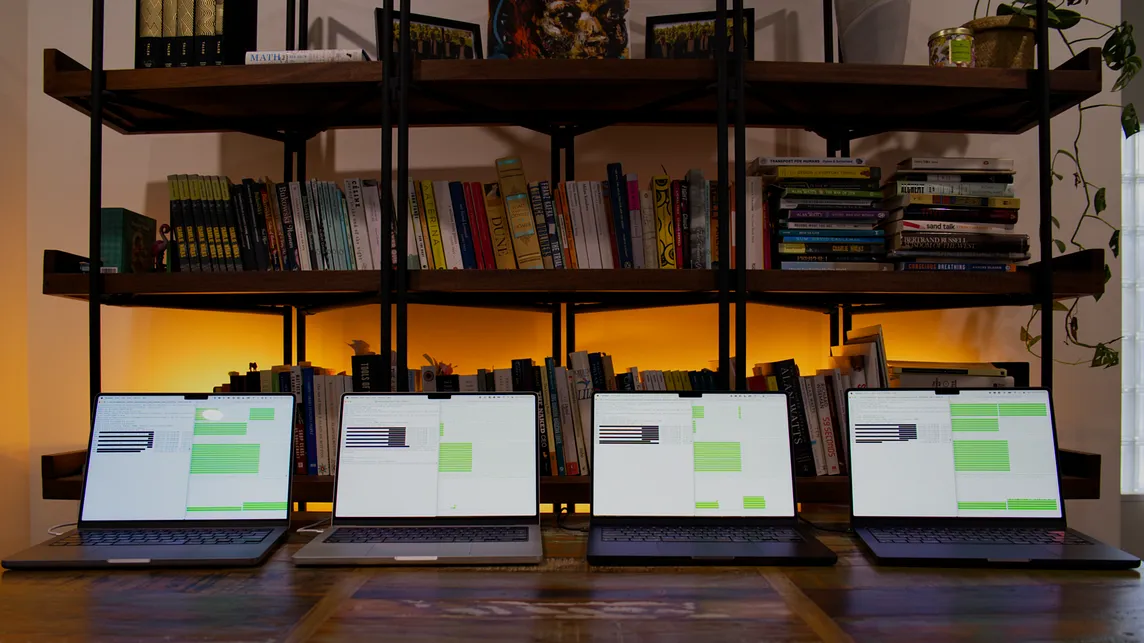Four laptops on a table in front of a bookcase running machine learning speed tests on their screen