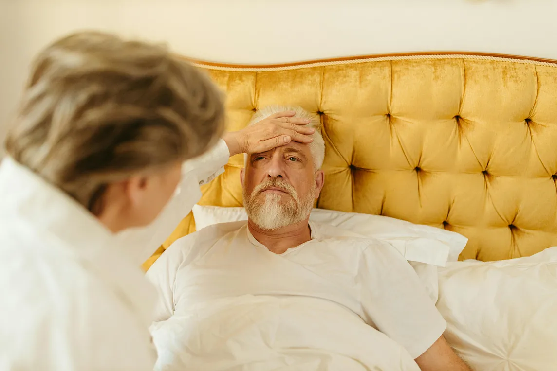 A photo of a man lying in bed with a woman feeling his forehead with her hand to see if he has a fever