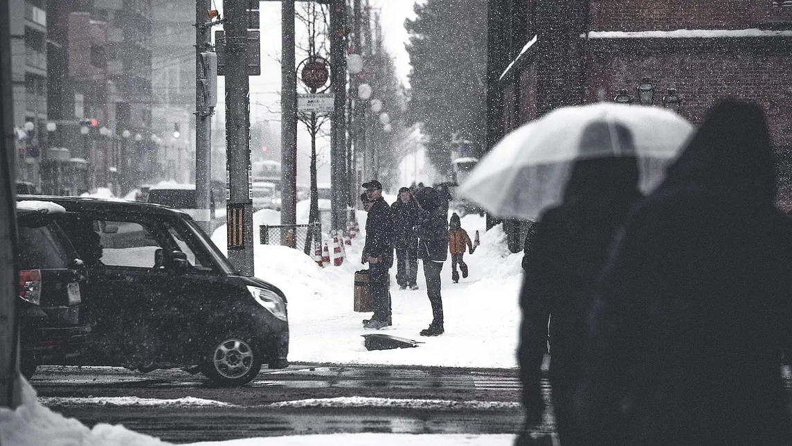 Snowy urban street scene with people walking under umbrellas, capturing the quiet stillness of winter — a visual reminder of the seasonal changes that can contribute to seasonal affective disorder (SAD) or seasonal depression. Discover ways to manage winter blues and embrace brighter days.