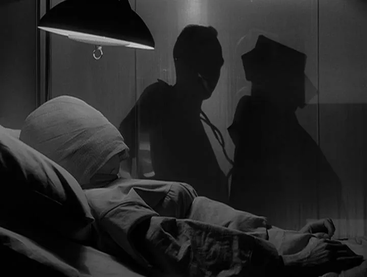 A woman sits in a hospital bed with her face wrapped in bandages while two shadowy figures stand in the background. Copyright Paramount.