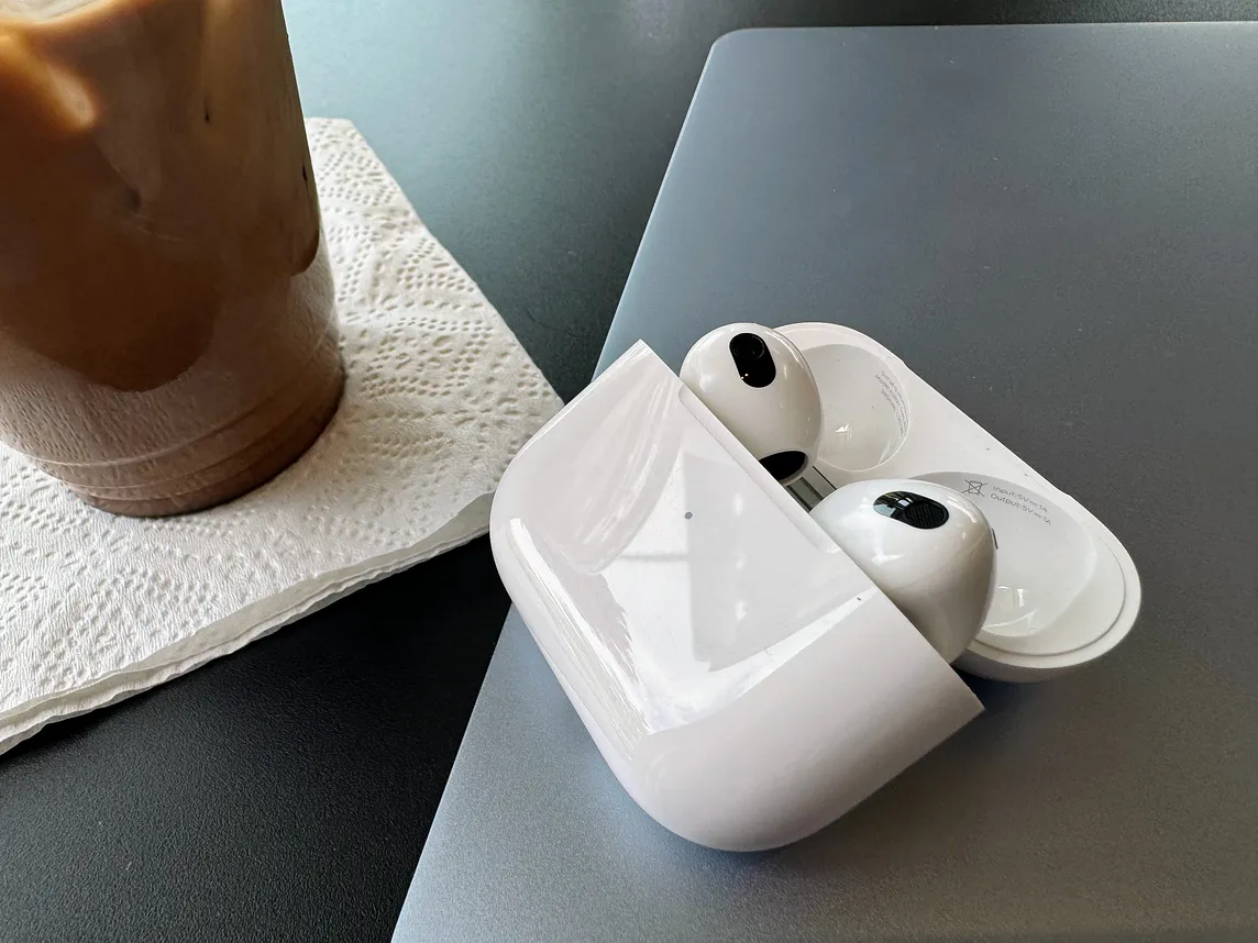 Apple’s 3rd Generation Air Pods in a case lying open on a laptop, next to a cup of iced coffee.
