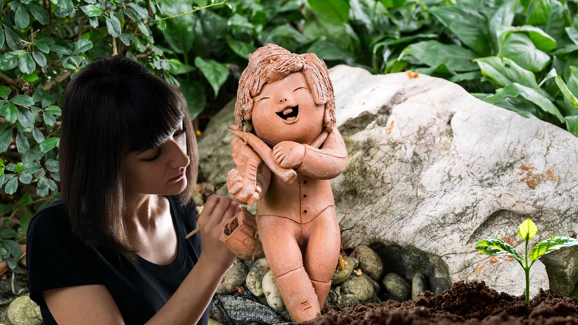 woman sculpting a clay child sculpture with seedling growing nearby