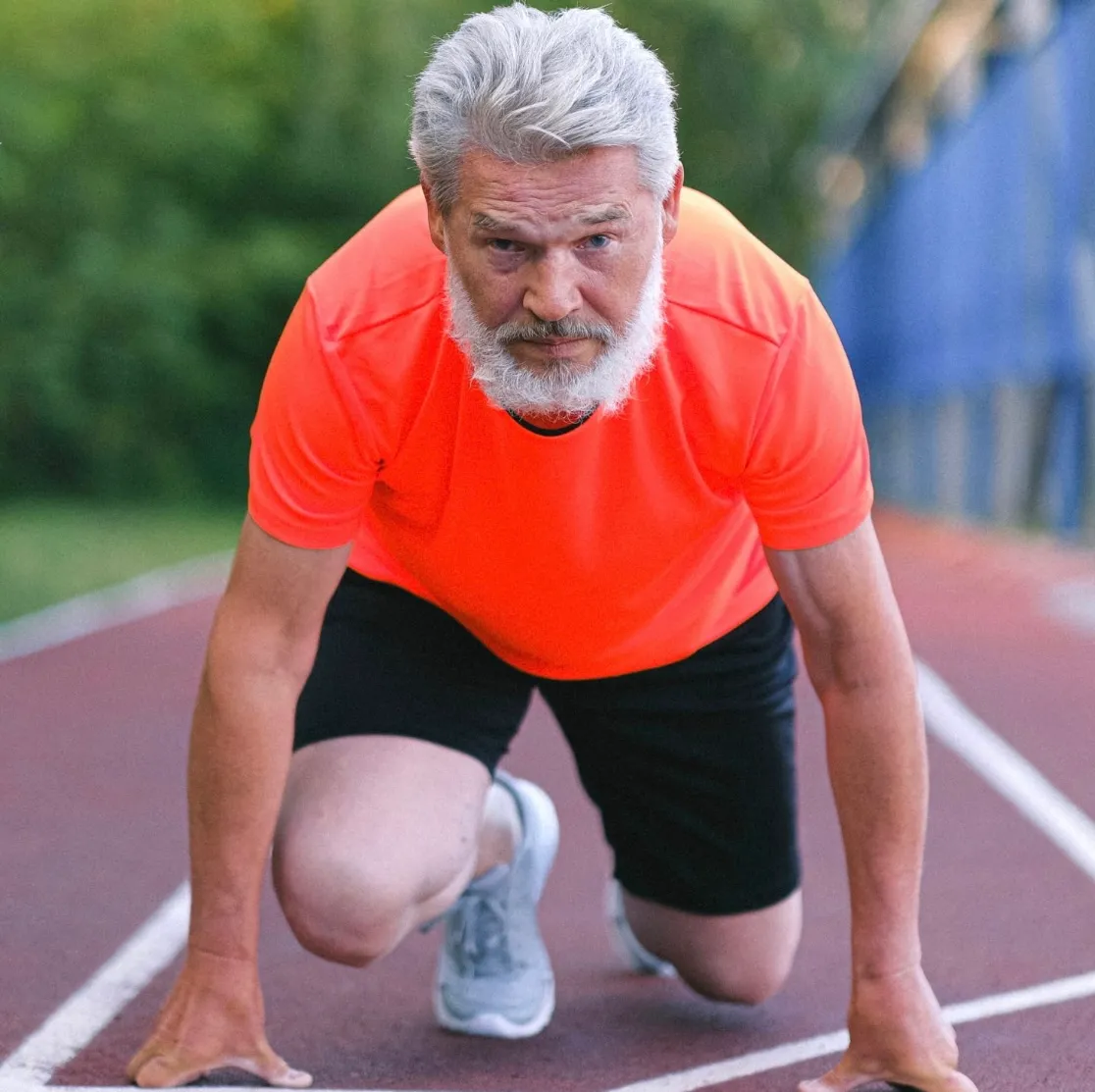 Older adult man in bright orange shirt in sprinting position .