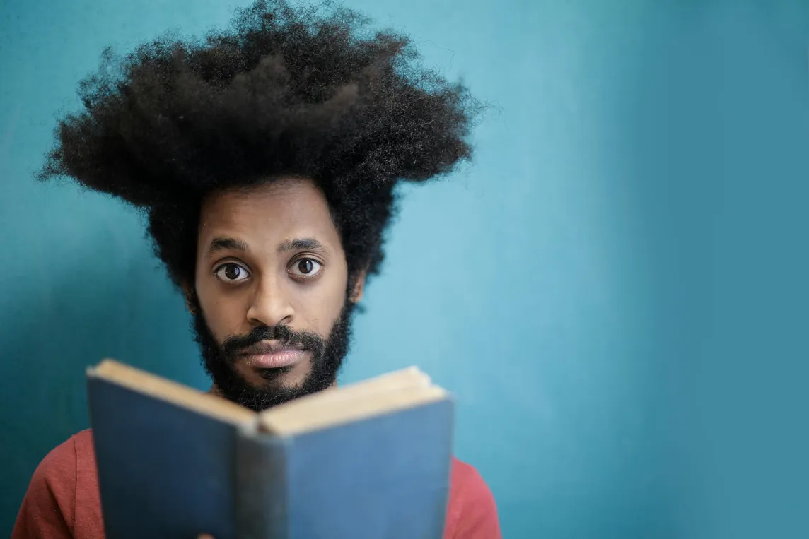 Color photo of a bearded African American man gazing at the viewer while holding an open book.