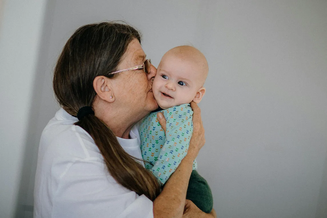 An older woman holding a baby and kissing them on the cheek