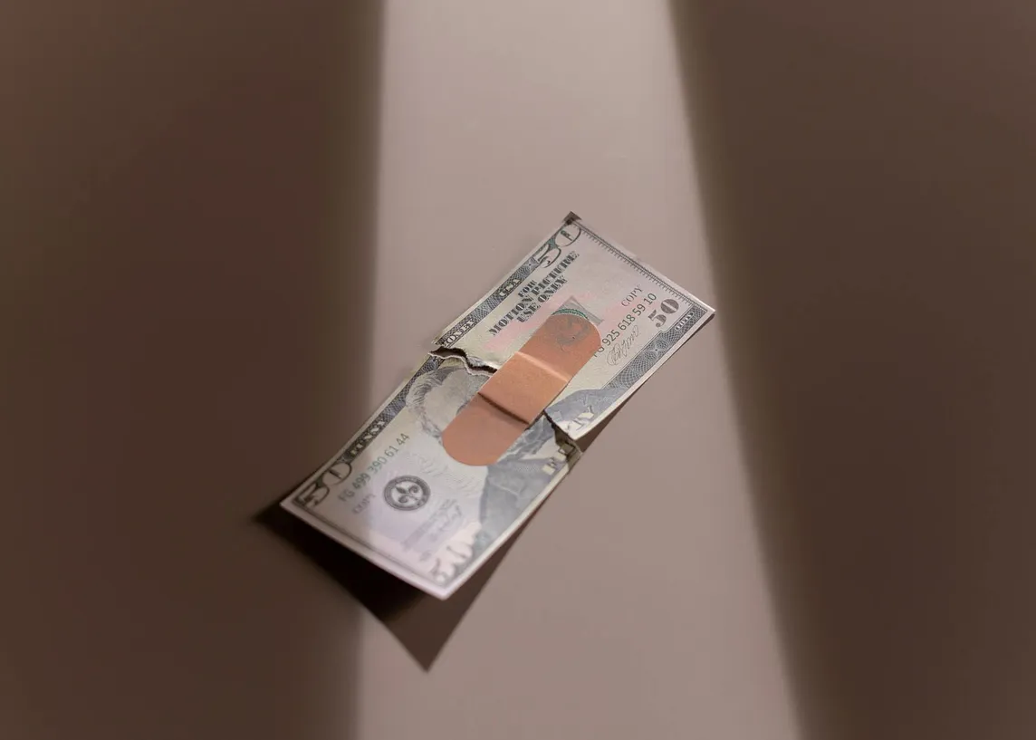 A U.S. fifty dollar bill is held together by a singular flexible fabric bandage.