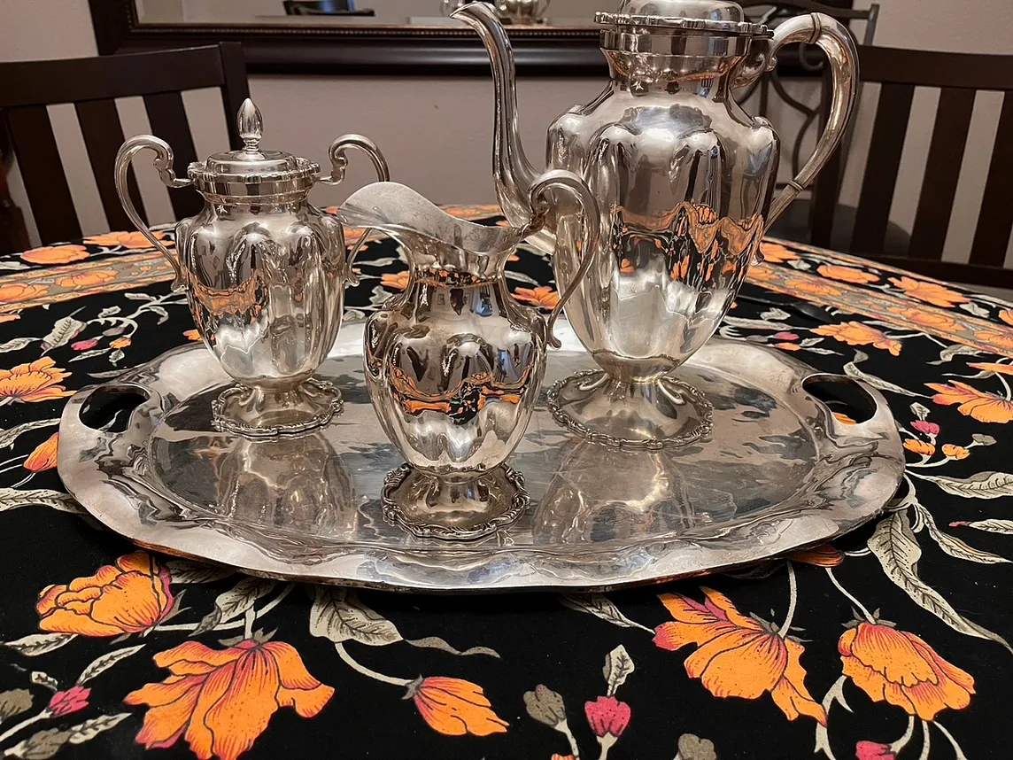 Silver coffee service sitting on a table with a flowered tablecloth.