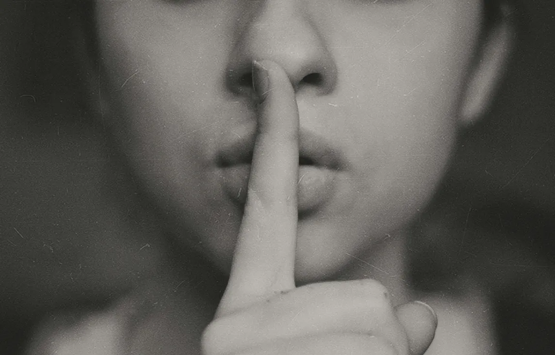Black and white photo of a woman shushing with index finger of lips.