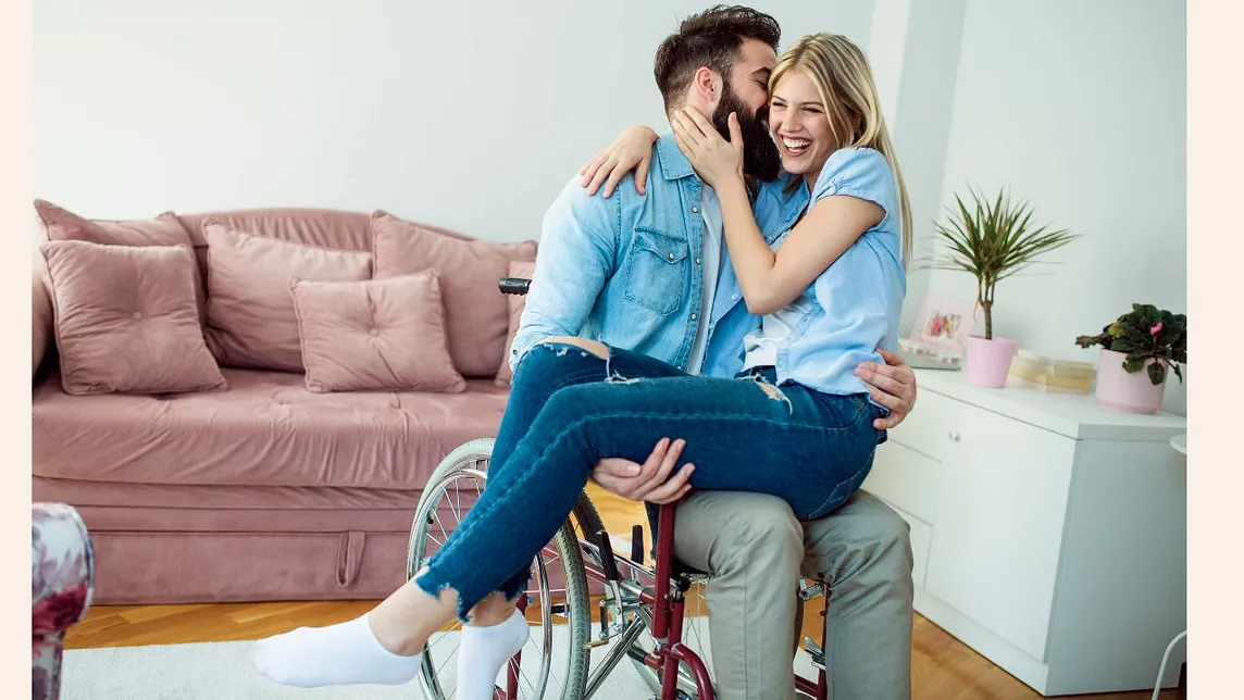 A man in a wheelchair kissing an abled woman sitting in his lap