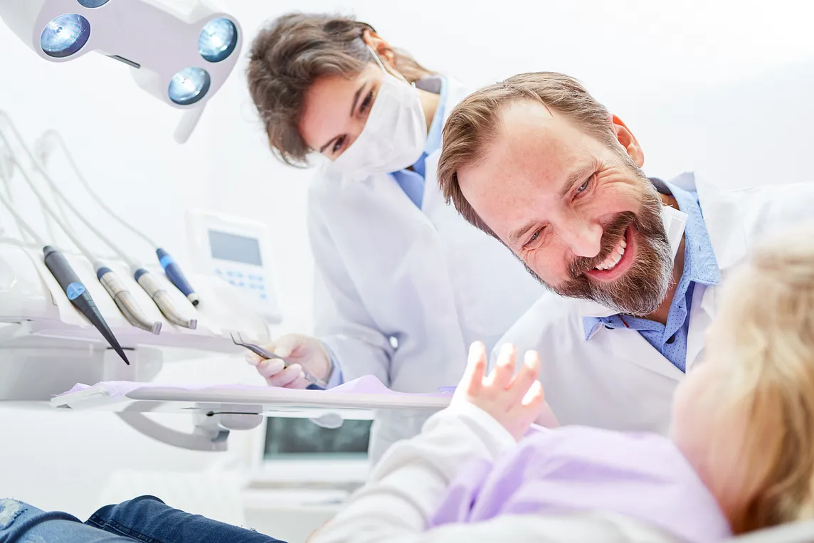 Stock image of a child in a dentist’s chair with a dentist and dental hygienist smiling while conversing with the child.