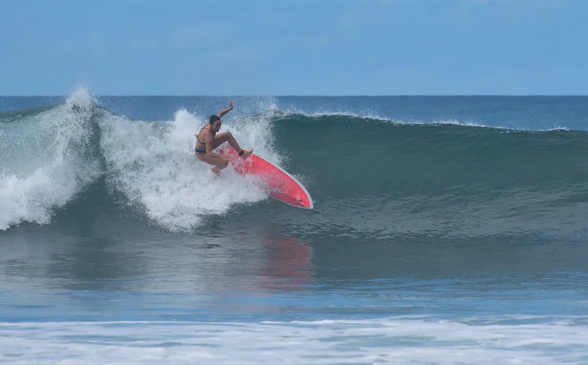 Girl and her surfboard falling off the top of a wave