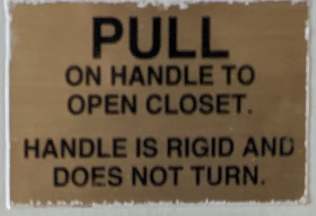 A sign reading ‘Pull on handle to open closet. Handle is rigid and doesn’t turn.’