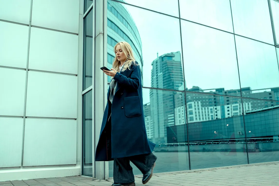 A woman walking in front of an office building while using her phone.