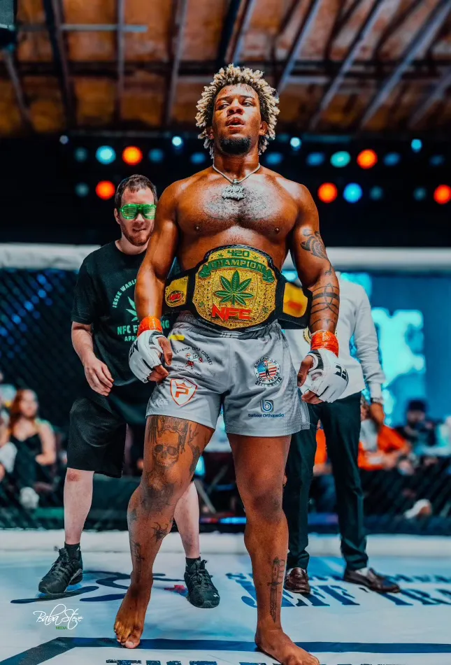 A man stands proudly wearing mma gloves and a championsip belt